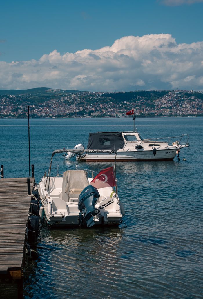 Two boats with Turkish flags docked in a scenic bay in Kocaeli, Turkey, under a clear blue sky.
